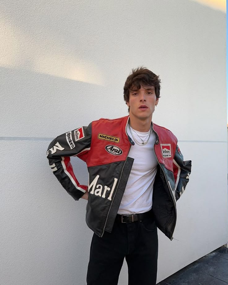 Person wearing a red and black jacket with various logos against a white wall.