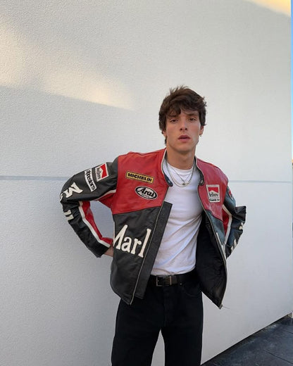 Person wearing a red and black jacket with various logos against a white wall.